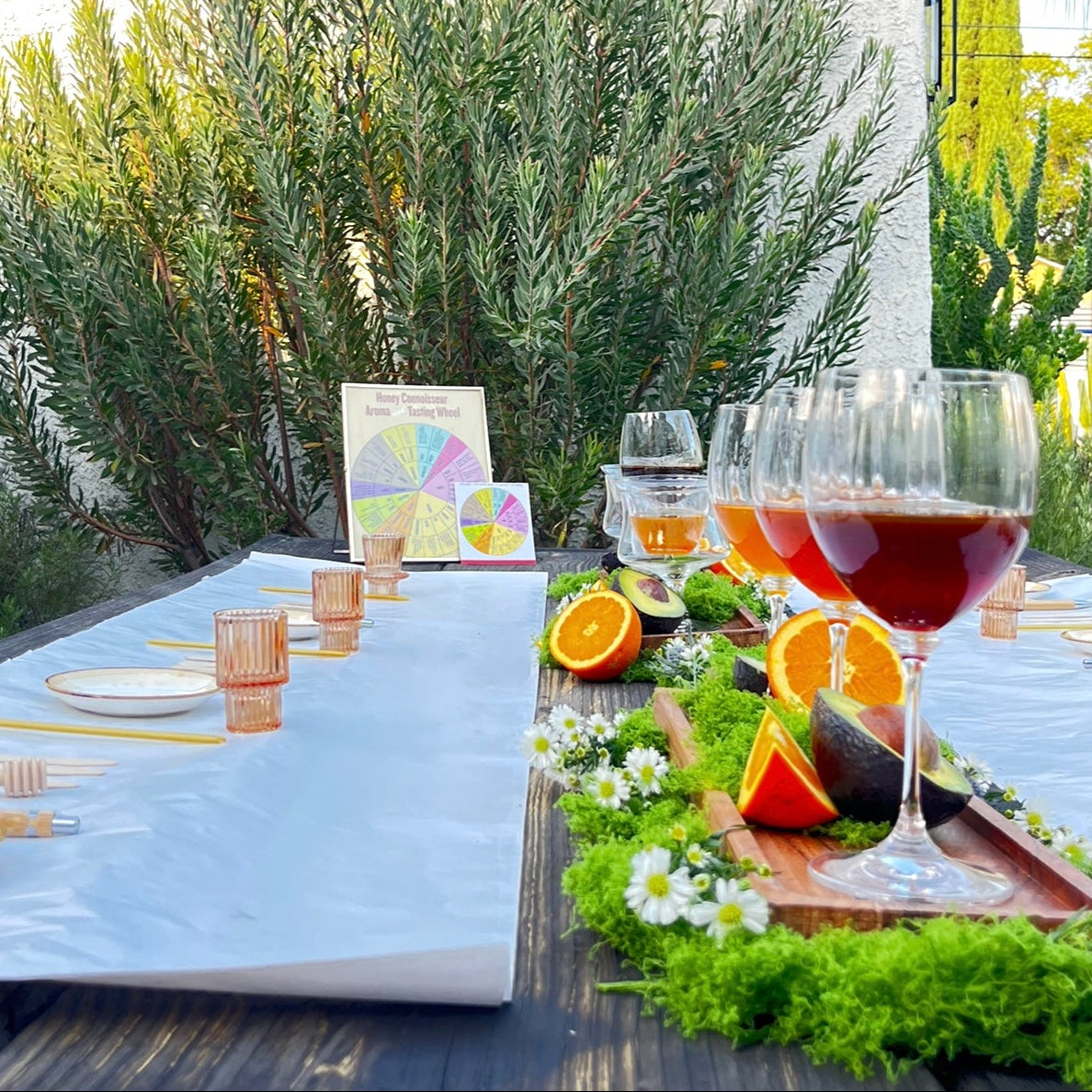 An outdoor honey tasting in Burbank California styled with a white table runner, clear glassware, copper-toned candle holders, and a greenery and citrus centerpiece.